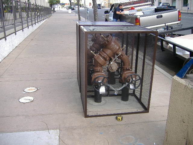 two customized cages being mounted to city sidewalk to protect six-inch backflow preventers
